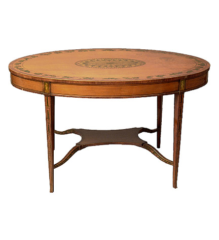 Edwardian satinwood oval center table, the top centering a painted reserve of feathers and an ivy border, raised on tapering square legs joined by stretchers centering a small shelf.