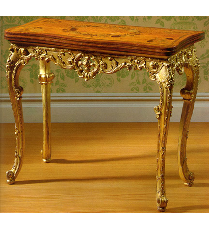 George III giltwood, satinwood and marquetry games table, the serpentine foldover top decorated with a floral wreath, opening to a brown suede playing surface, above a pierced acanthus-carved frieze over foliate and ribbon-twist carved cabriole legs ending in scrolled toes, regilt.