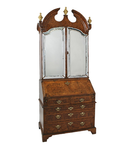 A fine and unusual George I burl walnut bureau-cabinet, the broken arched pediment above arched mirrored doors, the interior fitted with a removable compartment containing pigeon-holes, drawers and enclosed cupboard over a feather-strung lower section in two parts.  One interior drawer labelled in ink indistinctly 'Mr. WHITROD, Horseheath Lodge, nr. Linton, Cambs'.  Finials replaced.