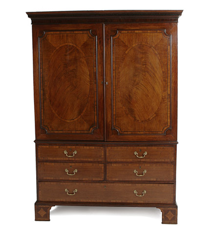 A George III mahogany linen press with a pair of oval paneled cupboard doors over two short and two long drawers and with a curved apron and  French bracket feet.