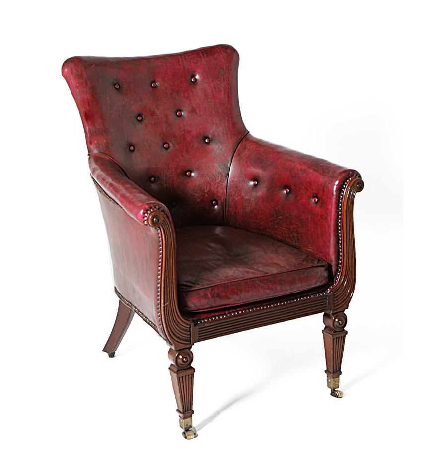 A George IV leather upholstered mahogany library chair with outscrolled arms and tapering legs ending in casters.