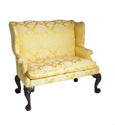 A George II upholstered carved mahogany wing-back settee, with lion-mask cabriole legs ending in paw feet.