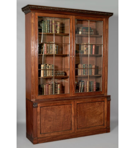 Tall pair of Regency mahogany bookcases with outset leaf carved pediment over two glazed doors, the base with panelled cupboard doors, molded borders throughout.