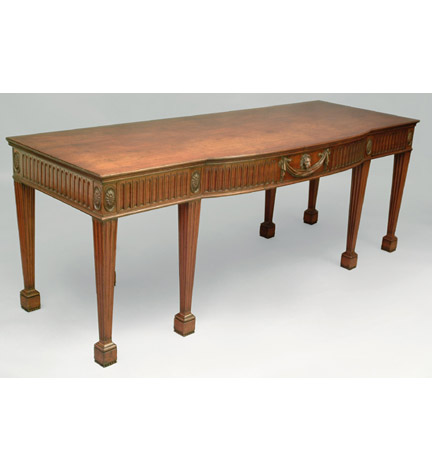 Bold George III mahogany large scale serving table in the Adams taste, of broken-bow outline, the frieze with deep fluting and centering a carved lion mask and swag, the six legs each headed by patera and ending in block feet.