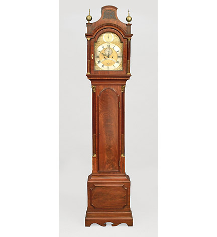 George III mahogany tall case clock with movement by Charles Louch, London.  The arched hood flanked by a pair of brass finials above stop-fluted colonettes; the case with an arched panelled door with conforming column decoration on a panelled base.