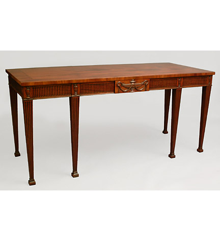 George III mahogany serving table in the Adam taste with banded and strung top over a fluted frieze centering a carved urn tablet and fitted with three blind drawers, raised on six tapering fluted legs ending in block feet.