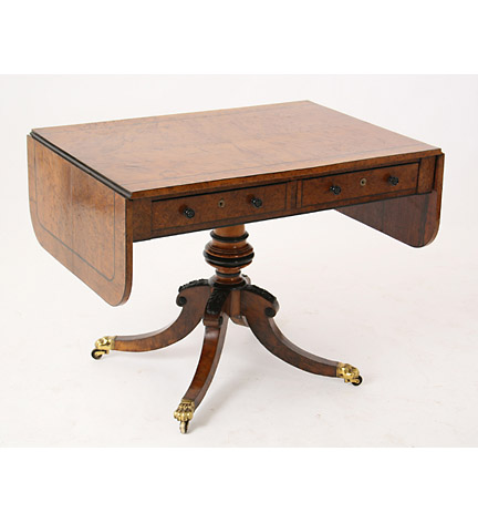 Regency burl oak sofa table fitted with two drawers and raised on a turned and part-ebonized pedestal ending in hipped quatropod supports with paw casters.