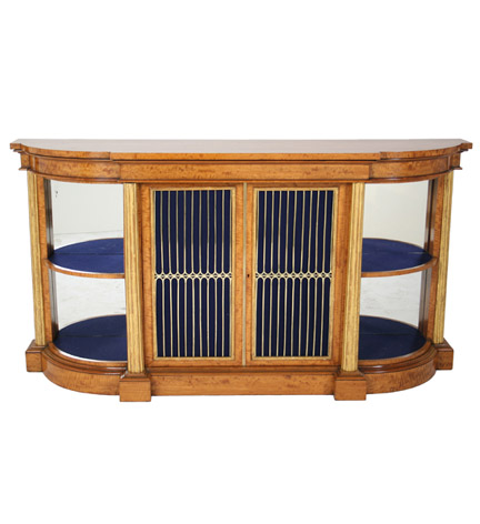 A Regency satinwood chiffonier of broken-bow outline with four giltwood reeded columns flanking the central pair of ormolu grilled doors and the open-shelved corner sections, all on a plinth base.